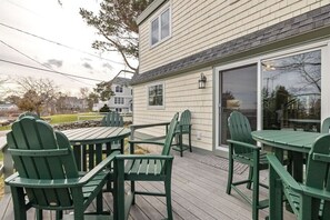 A deck with green Adirondack chairs and a table, overlooking a residential area with houses and a lawn.