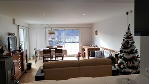 Una sala moderna con un sofá, un comedor con sillas y una mesa, un televisor y un árbol de Navidad.