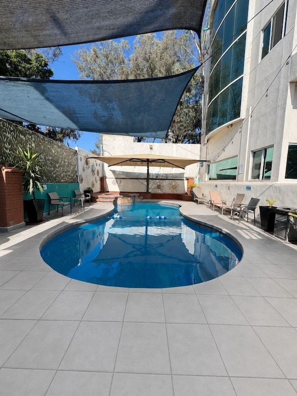 A swimming pool with a curved edge, surrounded by lounge chairs and a shaded area.