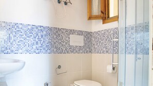 Een badkamer met toilet, bidet en wastafel, betegelde vloer en een douchecabine van glas.
