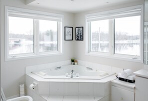 Une salle de bain moderne dotée d’une grande baignoire, de deux lavabos et de toilettes. De grandes fenêtres offrent une vue sur un paysage enneigé.