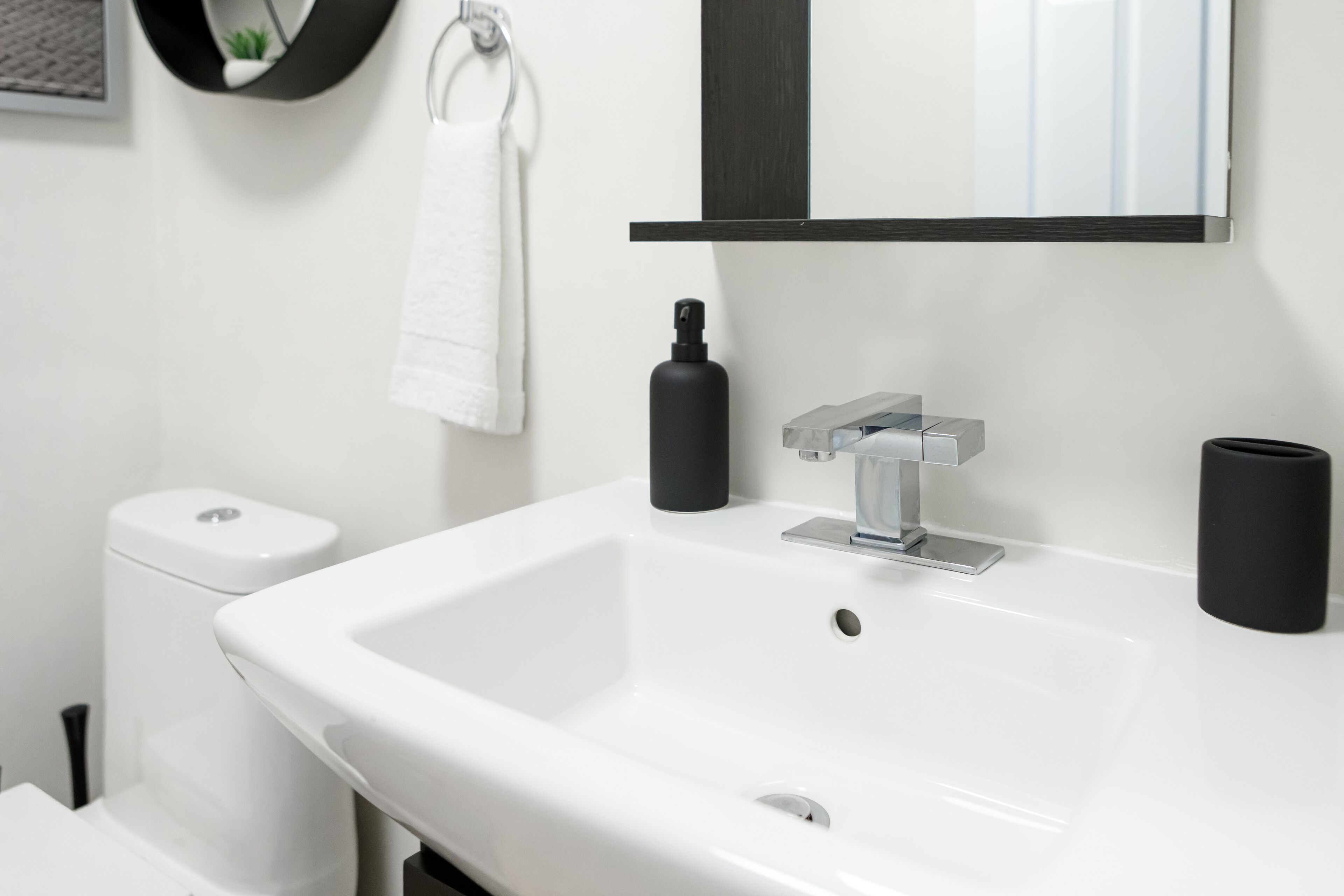 A modern bathroom with a white sink, a black soap dispenser, and a toilet.