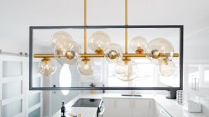 Een moderne keuken met een centraal eiland, witte kastjes en een hangende lamp met heldere glazen bolvormen en gouden accenten.