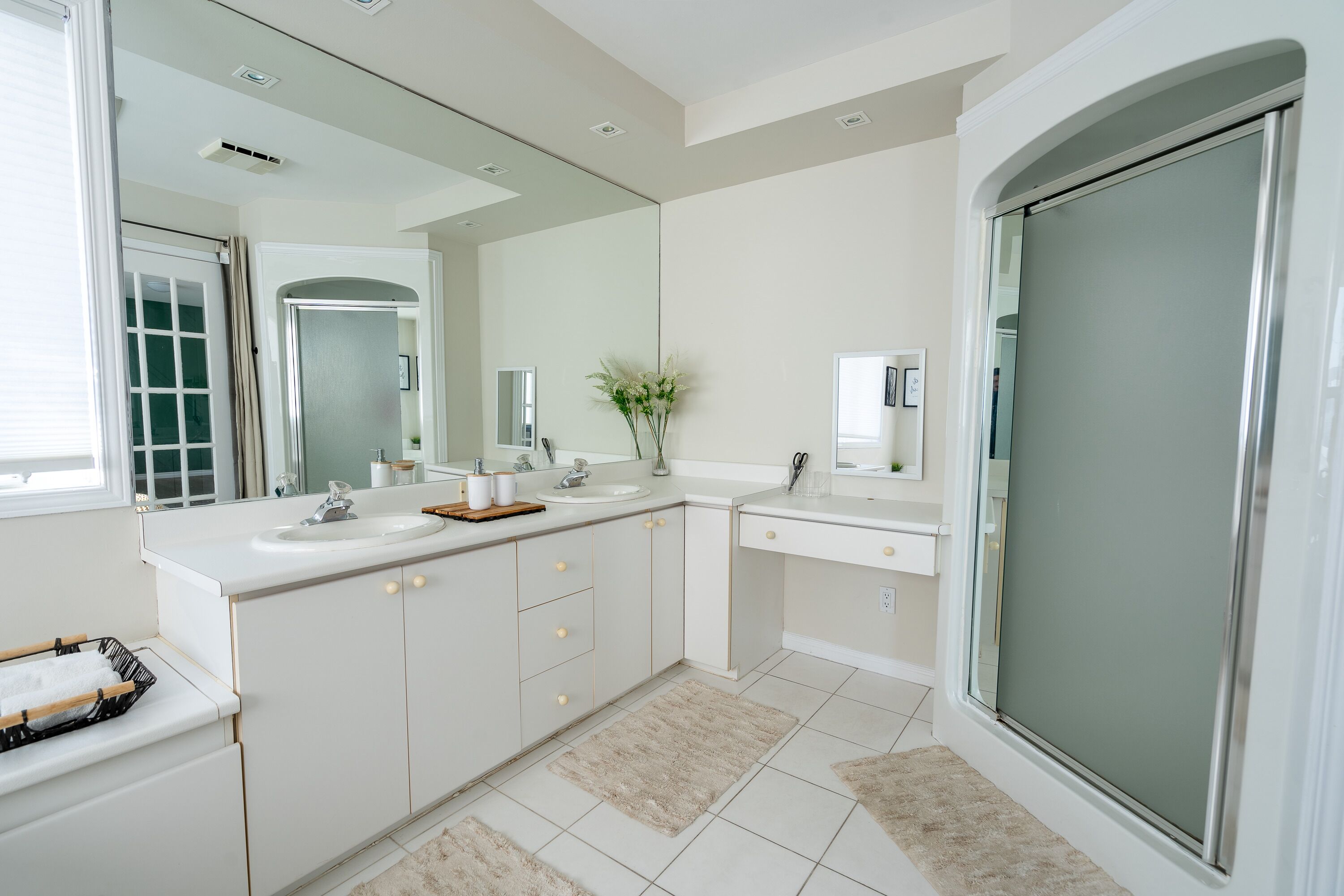 A modern bathroom with a large mirror, white cabinetry, a sink, and a shower area.