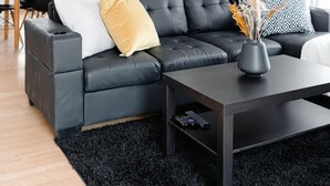 Een moderne woonkamer met een donker leren bank, een zwarte salontafel en een eethoek op de achtergrond.