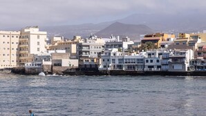 Paesaggio costiero con edifici lungo il lungomare e una persona che fa surf sullo sfondo.
