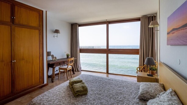 Una camera d'albergo con un letto grande, una scrivania, una sedia, un armadio e vista sul mare.