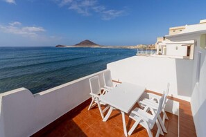 A terrace with a white table and chairs, overlooking the sea and a distant island. - HOUSE TOUCHING THE SEA 2. AMAZING VIEWS. (El Médano)