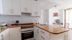 Una cucina moderna con mobili bianchi, un piano di lavoro in legno e un forno. È presente una zona pranzo con tavolo e sedie.