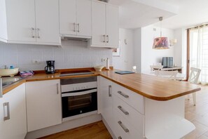 A modern kitchen with white cabinets, a wooden countertop, and an oven. There is a dining area with a table and chairs.