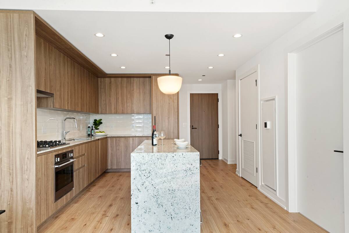 Une cuisine moderne avec des meubles en bois, un îlot en marbre et des spots encastrés au plafond.