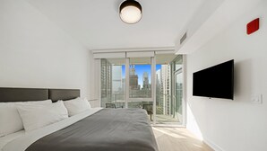 Un dormitorio moderno con una cama grande, televisión y un balcón con vistas a la ciudad.