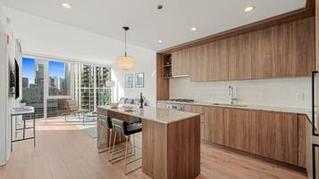 A modern kitchen with wooden cabinets, a central island, and a city view through large windows.