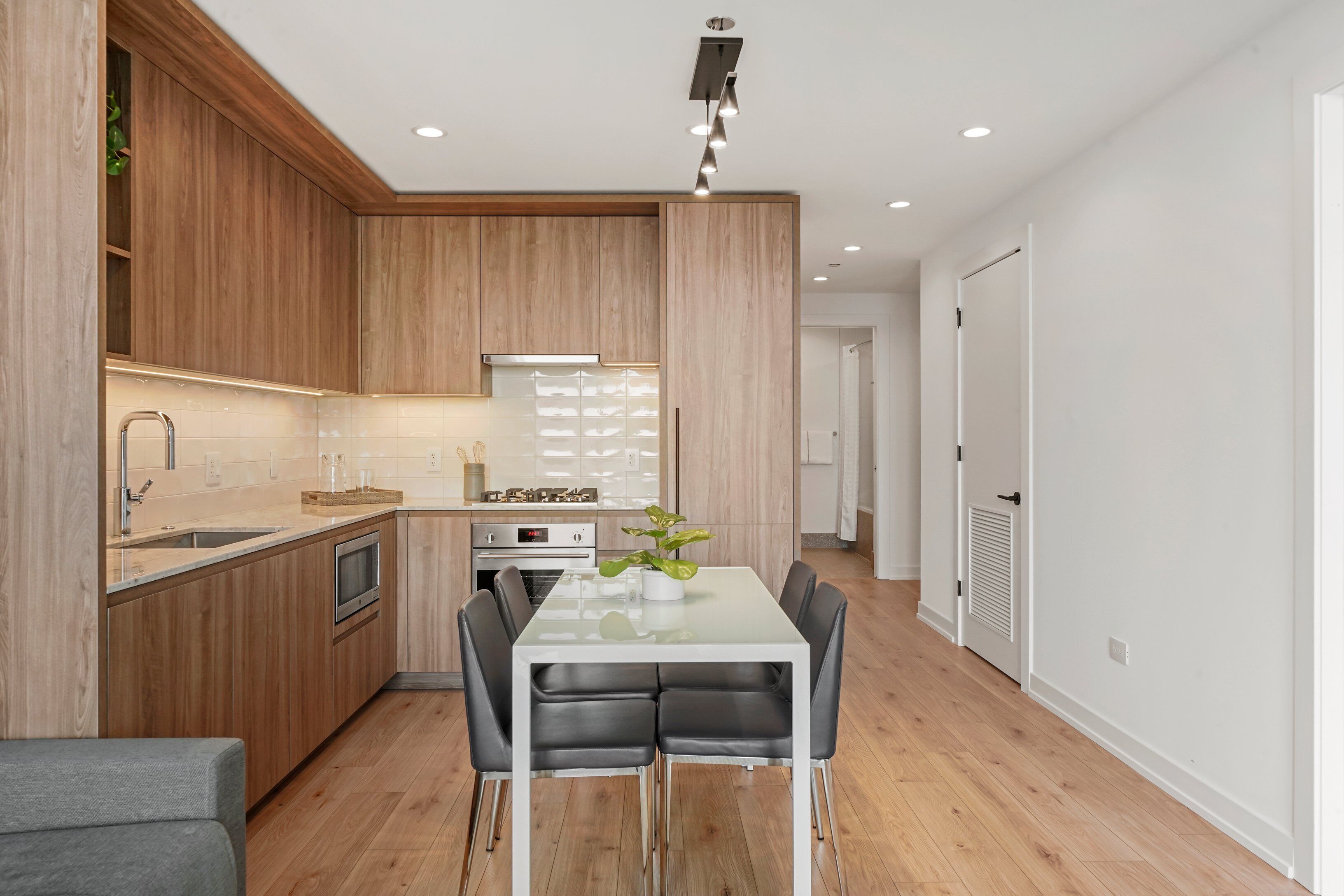 Een moderne keuken met houten kastjes, een witte eettafel en zwarte stoelen.