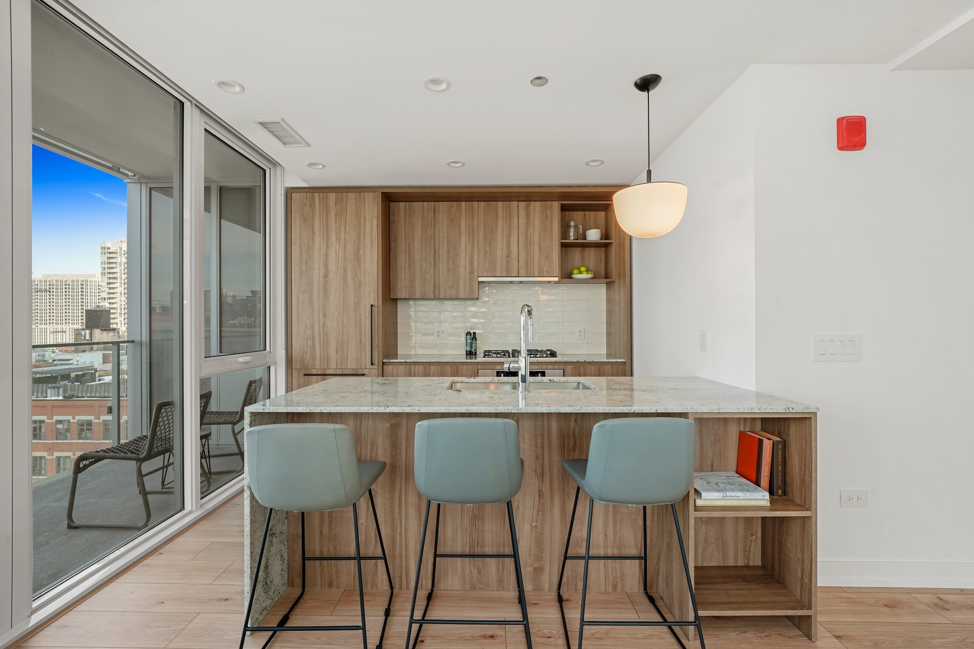 A modern kitchen with a large island, bar stools, and a view of the city through large windows.