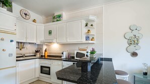 A modern kitchen with white cabinets, a granite countertop, and a dining area with stools. - Apartment for 4 with privileged access to the beach (Albufeira)