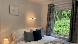 A neatly made bed with pillows, a bedside lamp, and a window with curtains. - Perfect Seaside Escape, Wifi Heated Indoor Pool Bar & Facilities near to St Ives (Lelant)