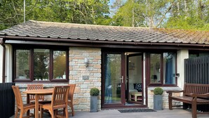 A stone building with a tiled roof, numbered 230, featuring a patio with wooden furniture and a small garden. - Perfect Seaside Escape, Wifi Heated Indoor Pool Bar & Facilities near to St Ives (Lelant)