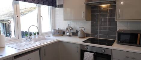 Una cocina moderna con armarios blancos, salpicadero de azulejos negros, horno empotrado y una ventana con vistas a una casa.