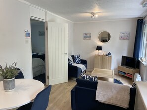 A compact living space with a dining table, a sofa, a TV, and a small kitchen area.