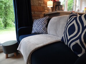 A cozy living room with a dark blue sofa, a patterned throw pillow, and a small round ottoman.