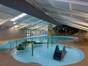 An indoor swimming pool with slides and a rock formation backdrop.