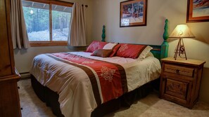 Quarto com cama, mesa de cabeceira, luminária, janela com cortinas e um quadro na parede.