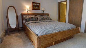 A bedroom with a wooden bed, a full-length mirror, two bedside lamps, and a door. - Cozy Condo close to the Chair Lift (Angel Fire)