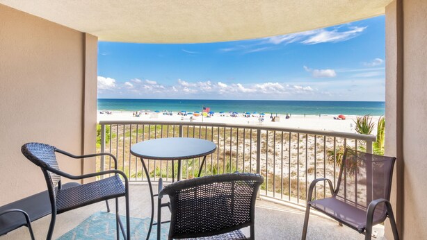 Un balcon donnant sur une plage, avec une table ronde et deux chaises en osier.