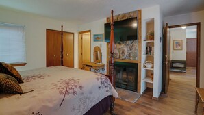 A bedroom with a four-poster bed, a stone fireplace, and a wooden door leading to another room.