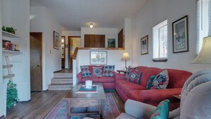 A living room with a red sofa, a coffee table, and a patterned rug. There is a staircase leading to an upper level.