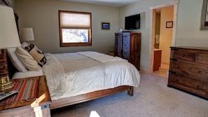 Een slaapkamer met een bed, een dressoir, een televisie en een raam.