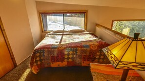 Um quarto com cama, janela, luminária e vista para uma paisagem nevada.