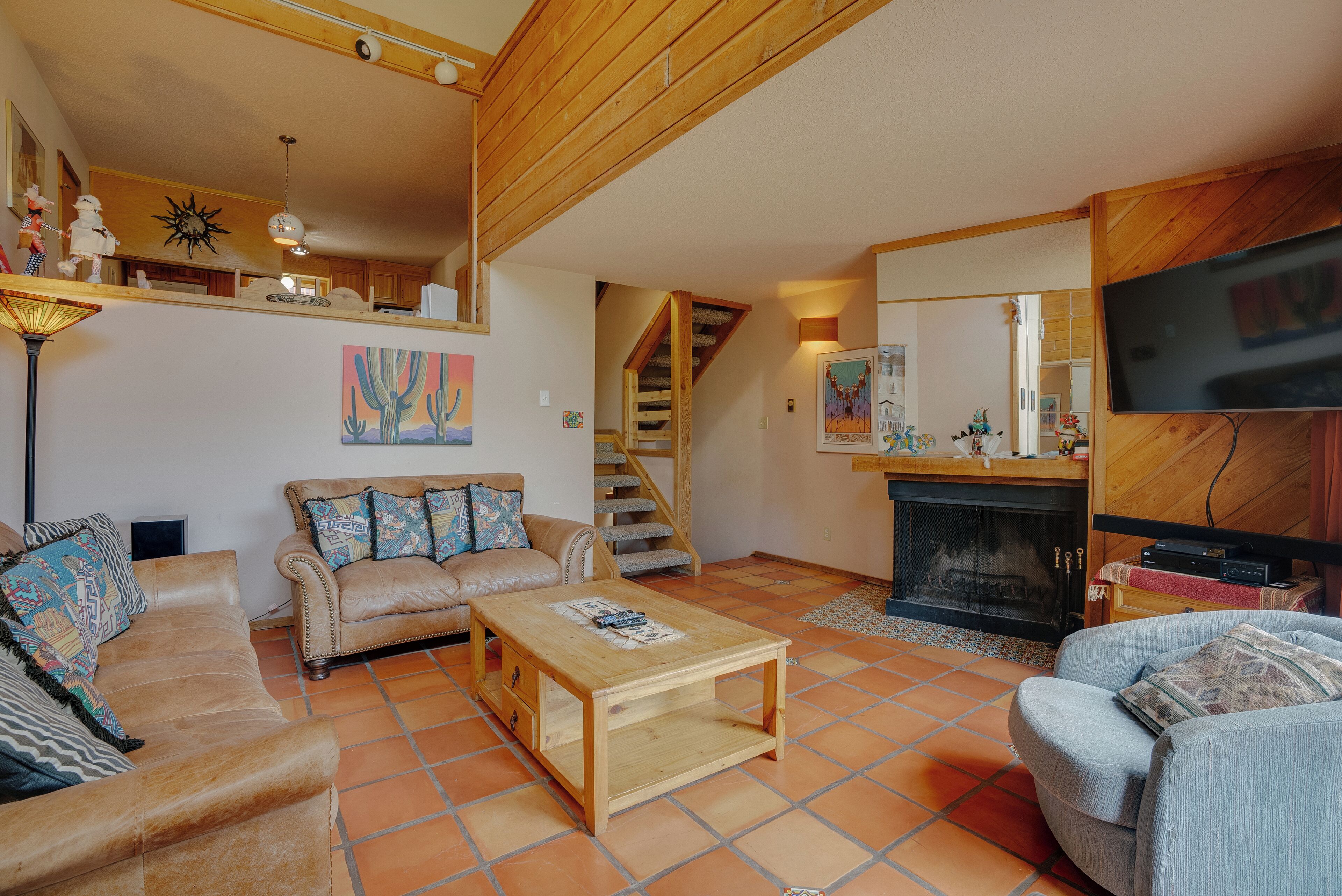 A living room with a wooden coffee table, two sofas, a fireplace, and a TV mounted on the wall.