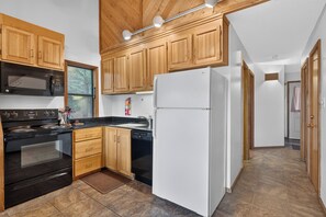 Une cuisine avec des meubles de rangement en bois, un four noir, un réfrigérateur blanc et un micro-ondes noir.