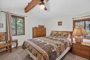A bedroom with a wooden bed, a nightstand, a dresser, a ceiling fan, and a window with a view of trees.