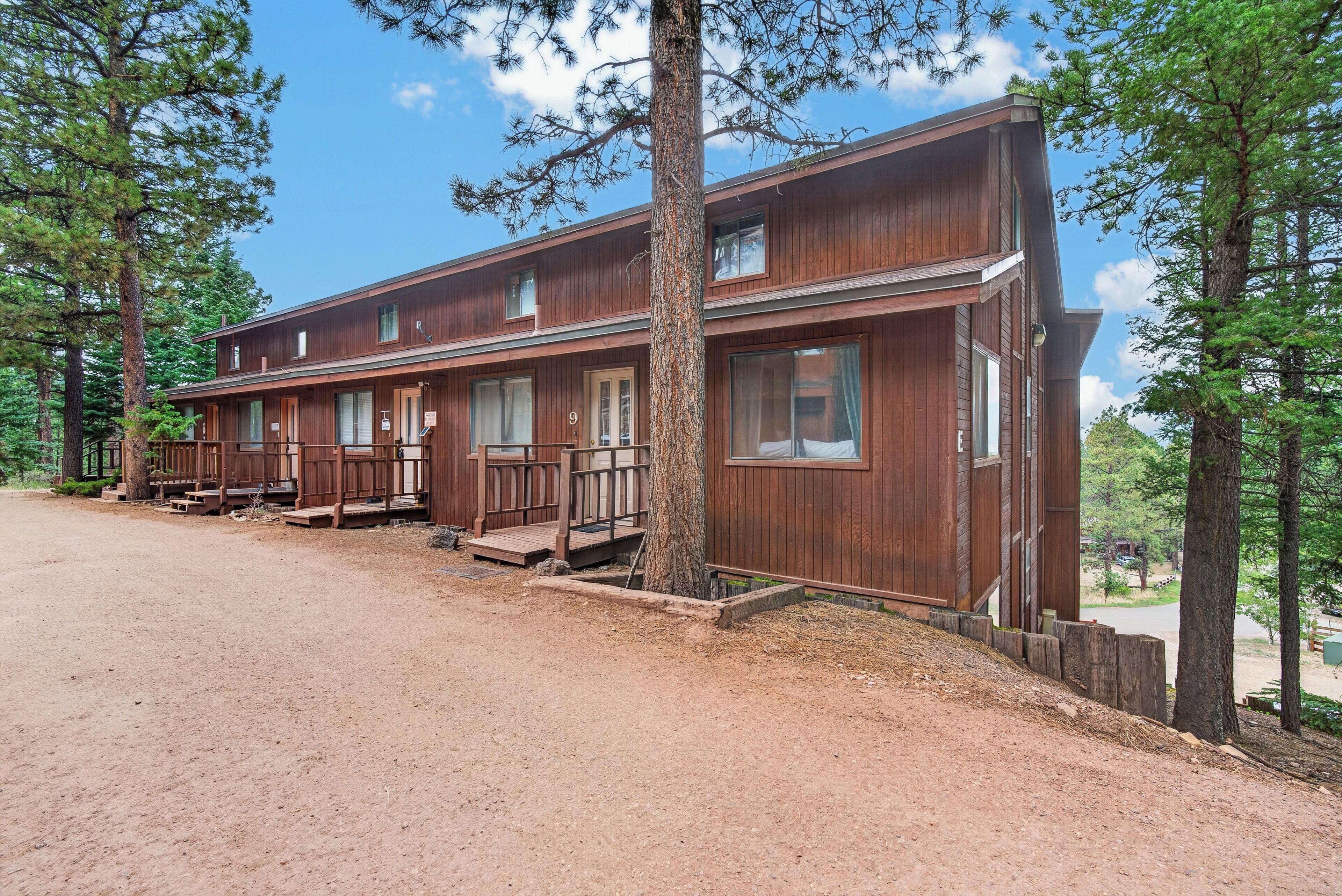 A two-story wooden cabin with a porch and a dirt driveway.