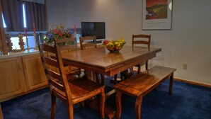 Un coin repas avec une table en bois, des chaises, un panier de fruits et un chandelier.