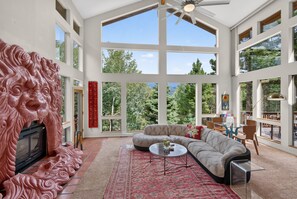 A spacious living room with a large window, a fireplace, and a decorative lion head sculpture.