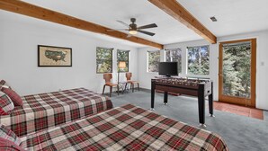 A room with two beds, a ceiling fan, a television, and a foosball table. - Home with Great Views of the Angel Fire Ski Mountain and Valley (Angel Fire)