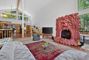 Un salón amplio con una televisión grande, una chimenea con una escultura de león y una zona de comedor con mobiliario de madera.