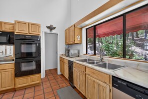 A kitchen with wooden cabinets, a built-in oven, a microwave, and a window with a red awning.