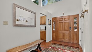 A hallway with a wooden bench, a large mirror, a door with glass panels, and a patterned rug. - Home with Great Views of the Angel Fire Ski Mountain and Valley (Angel Fire)