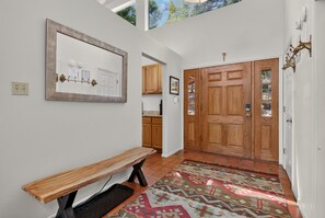 A hallway with a wooden bench, a large mirror, a door with glass panels, and a patterned rug. - Home with Great Views of the Angel Fire Ski Mountain and Valley (Angel Fire)