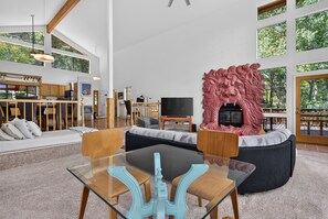A modern living room with a glass coffee table, a fireplace with a lion sculpture, and a large window offering a view of trees. - Home with Great Views of the Angel Fire Ski Mountain and Valley (Angel Fire)