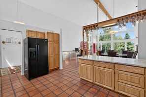 Een moderne keuken met een zwarte koelkast, houten kastjes en een groot raam met uitzicht op groen.