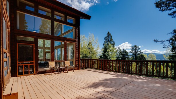 Una terraza de madera con un espacio acristalado, una silla y vistas a árboles y montañas.