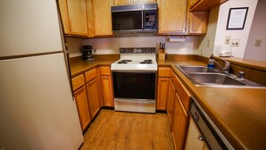 Una cocina compacta con armarios de madera, un lavamanos de acero inoxidable y un microondas integrado.
