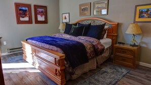Une chambre à coucher avec un lit en bois, une literie à motifs, une table de chevet avec une lampe et des œuvres d’art encadrées accrochées au mur.