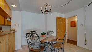 Un espace repas comprenant une table en bois et des chaises en métal, un lustre, ainsi qu’un coin cuisine avec des meubles en bois et un plan de travail.